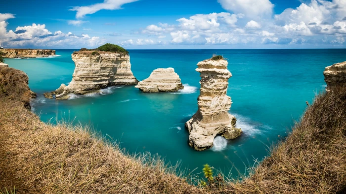 rock monolith surrounded by body of water under blue sky Torre puglia italy 2k