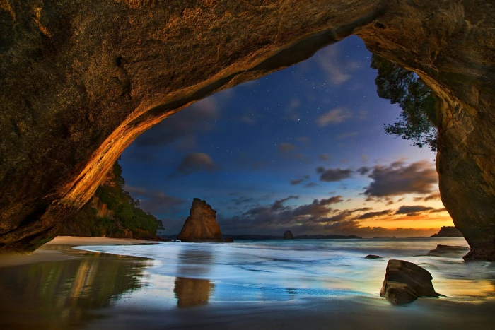 calm body of water under brown cave beach sea sunset clouds 2k