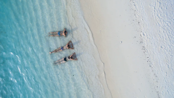 three people sunbathing on shoreline women wearing bikinis lying beach 2k 4k
