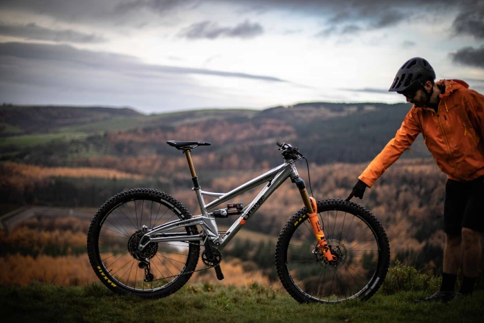 man standing and touching gray full suspension bike outdoors 2k 4k 5k