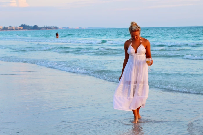 woman in white halter strap dress walking on seashore during daytime 2k 4k 5k