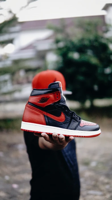 selective focus photo of person holding unpaired black and red Nike Air Jordan 1 shoe 2k