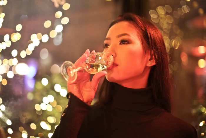 Young Adult Woman Drinking Wine in a bar with xmas bokeh lights around her 2k