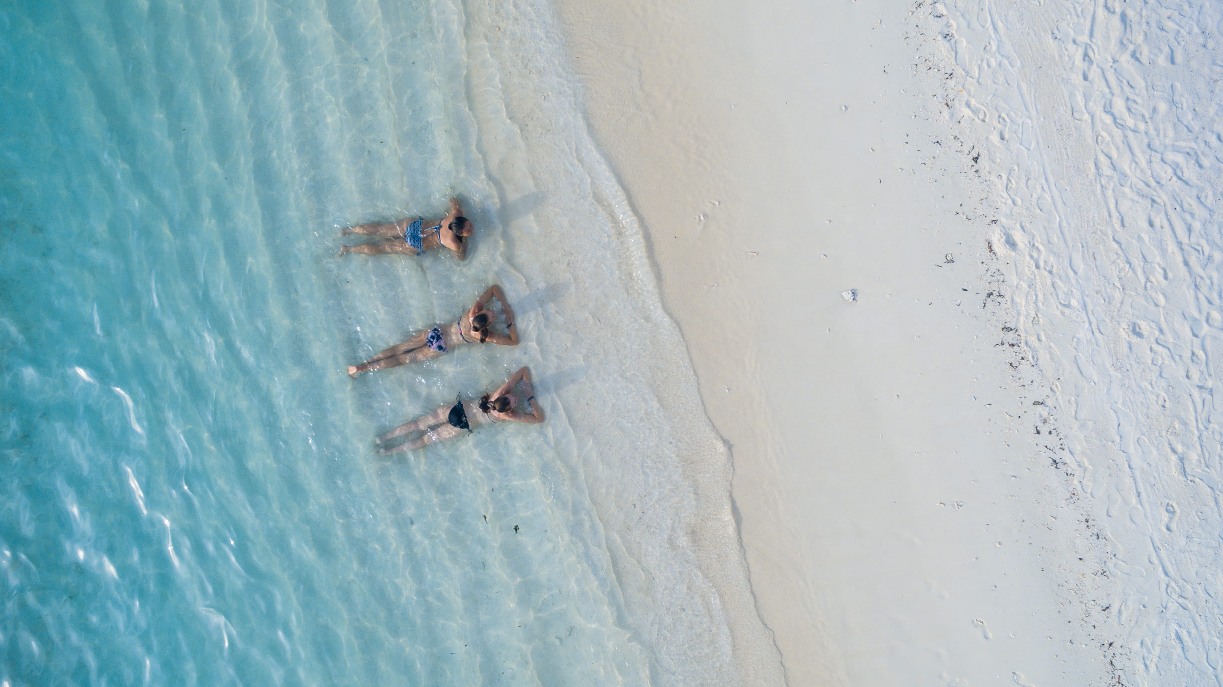 three people sunbathing on shoreline women wearing bikinis lying beach 2k 4k
