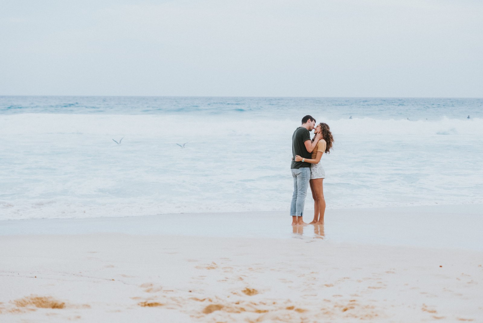 man and woman kissing each other on the seashore near beach 2k 4k 5k