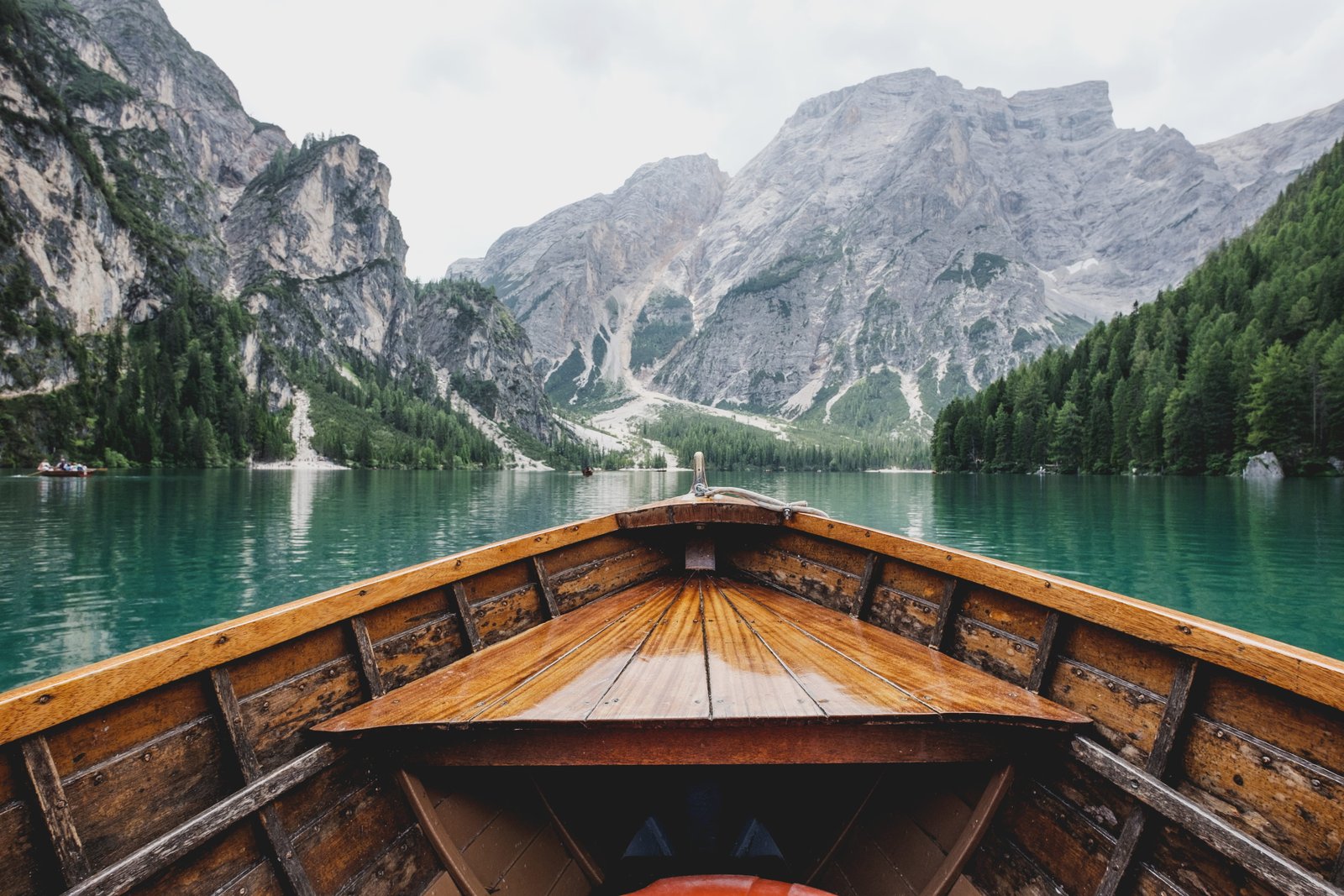 brown wooden boat moving towards the mountain person riding on lake during daytime 2k 4k 5k