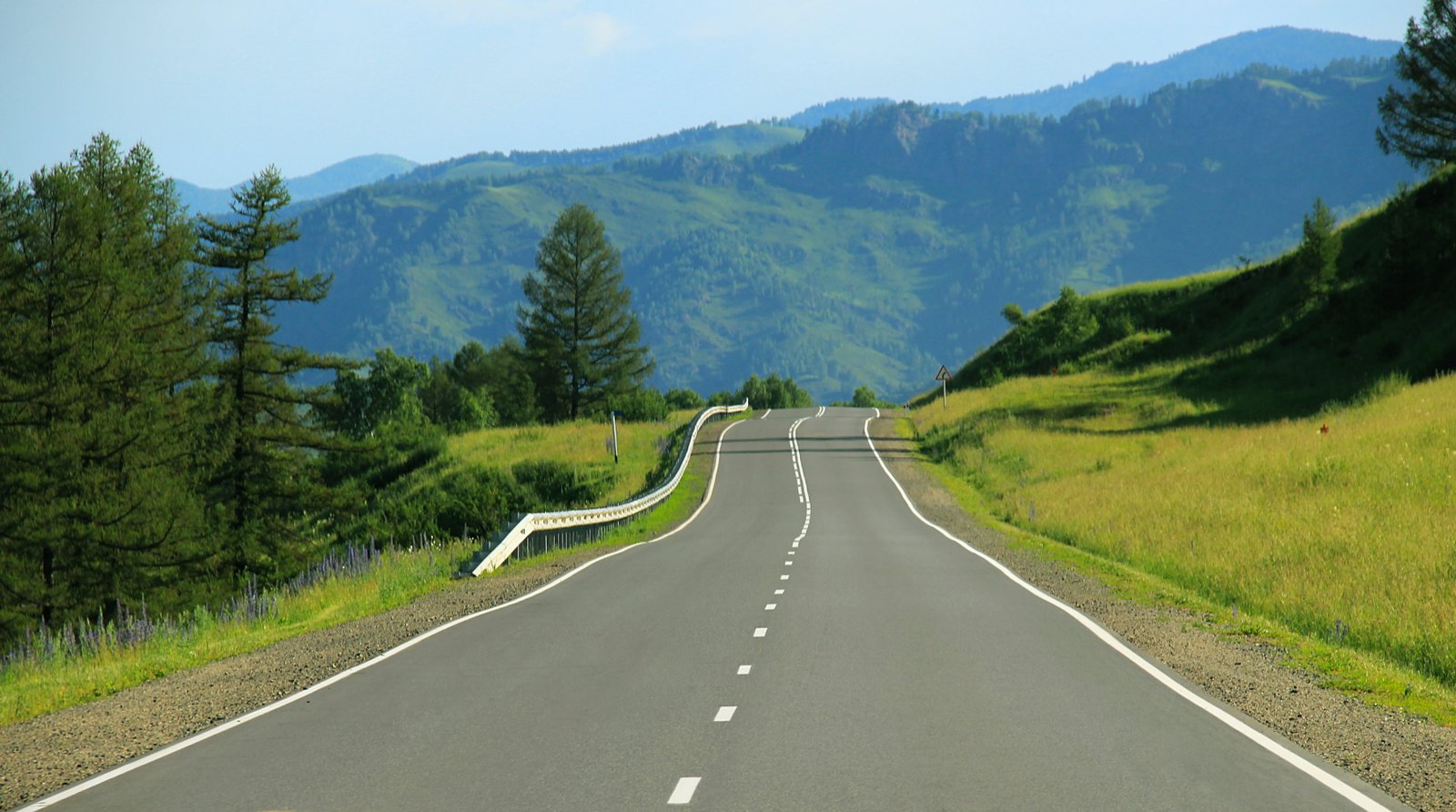 gray concrete road on between green grass and trees near mountain at daytime 2k 4k 5k