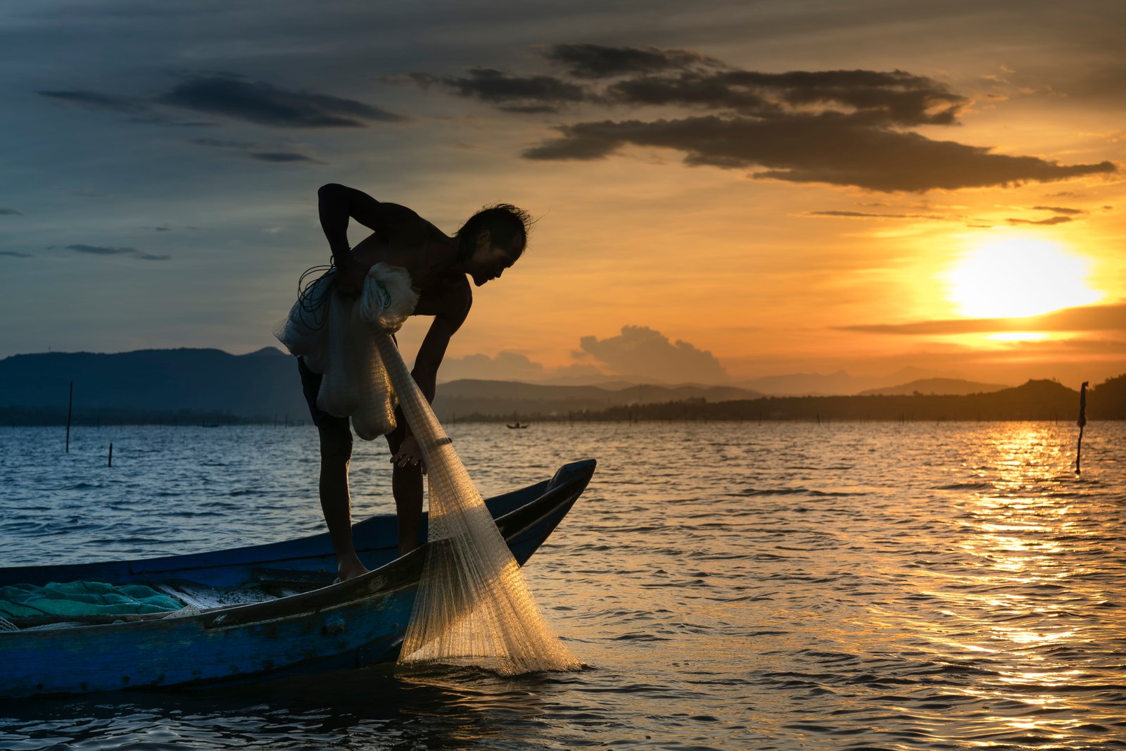 Man on Boat Holding White Mesh Fishing Net backlit beach clouds 2k 4k 5k 8k