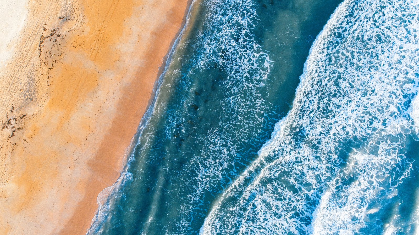 seawaves beside brown sand aerial photography of ocean wave 2k 4k