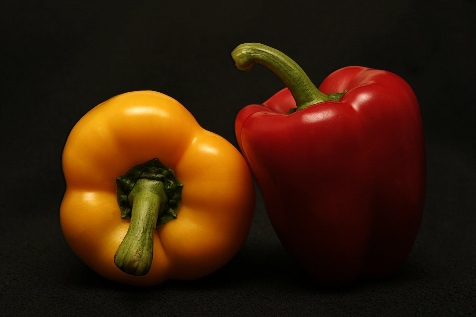 two red and yellow bell peppers black surface food cook spice 2k