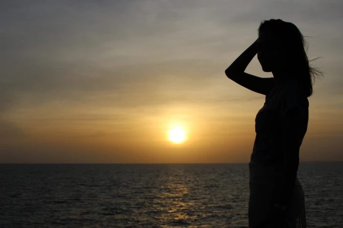 Silhouette of the profile a slim young woman by sea at sunset 2k
