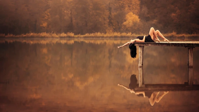 women's black dress woman lying on wooden dock near body of water during daytime 2k