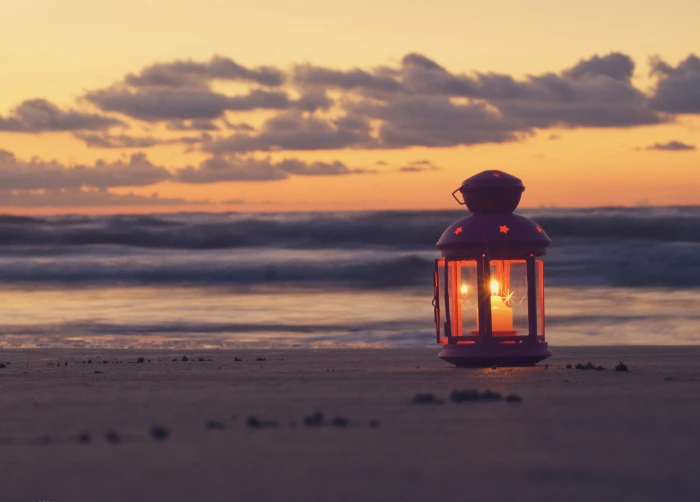 white pillar candle with lantern sand sea beach the sky clouds 2k