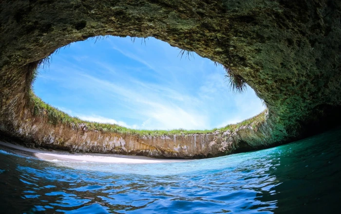 body of water with cave during daytime beach island sand grass 2k