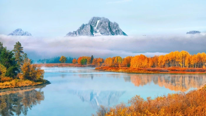 brown trees and blue body of water gray mountains covered with white clouds during daytime 2k