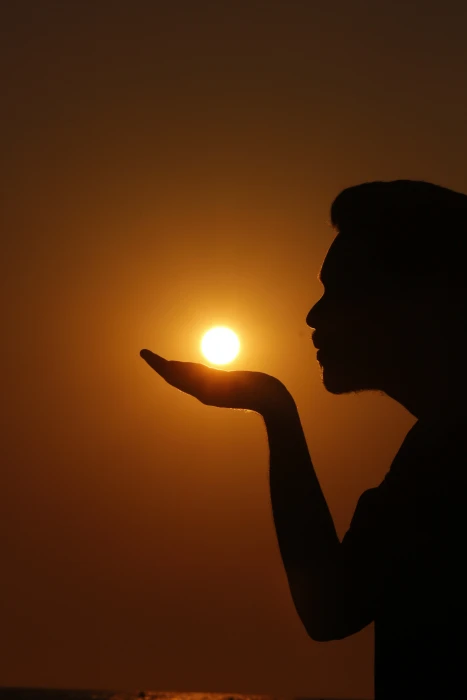 silhouette of a person as if he she is summoning the sun on his her hand 2k