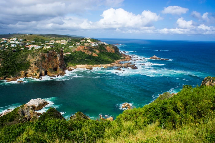 brown rock formation covered by green grass beside blue sea under and white sky 2k