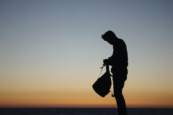 silhouette of man holding backpack during orange sunset photo bag 2k 4k