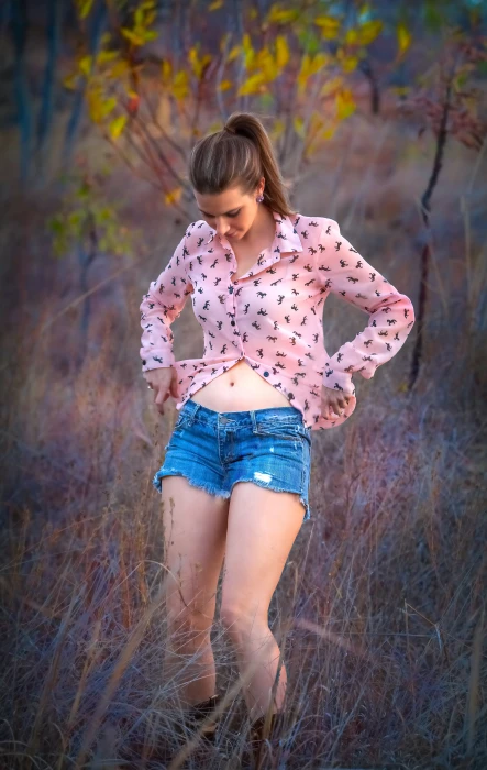 woman wearing pink dress shirt and blue denim cut off shorts standing on grass during daytime 2k