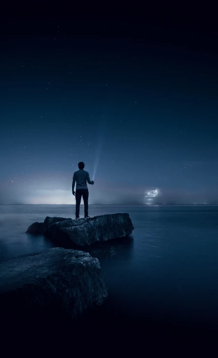 man standing on rock surrounded by water holding a flashlight pointing at the sky 2k 4k