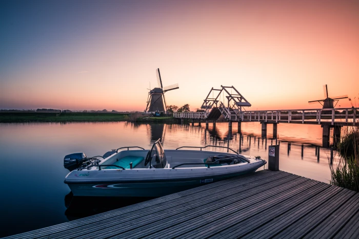 white and teal motorboat beside brown wooden walk way bridge during sun set kinderdijk holland 2k 4k 5k