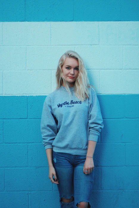 woman in teal sweater and blue jeans leaning on white wall 2k
