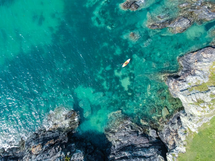 aerial view of boat on sea beside rock formation at daytime white body water surrounded gray concrete mountain rocks 2k 4k