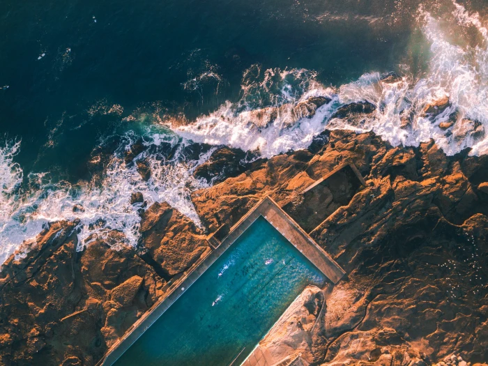 brown cliff aerial view photography of swimming pool near sea at daytime 2k 4k