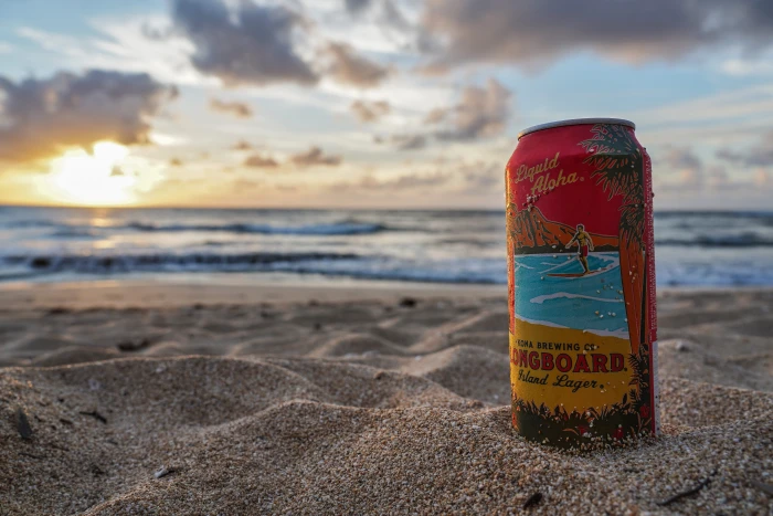 Longboard beverage can on sand by the beach during day tin beer 2k 4k 5k 8k