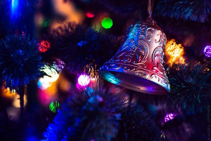 silver bell ornament closeup photography of Christmas tree with string lights turned on 2k