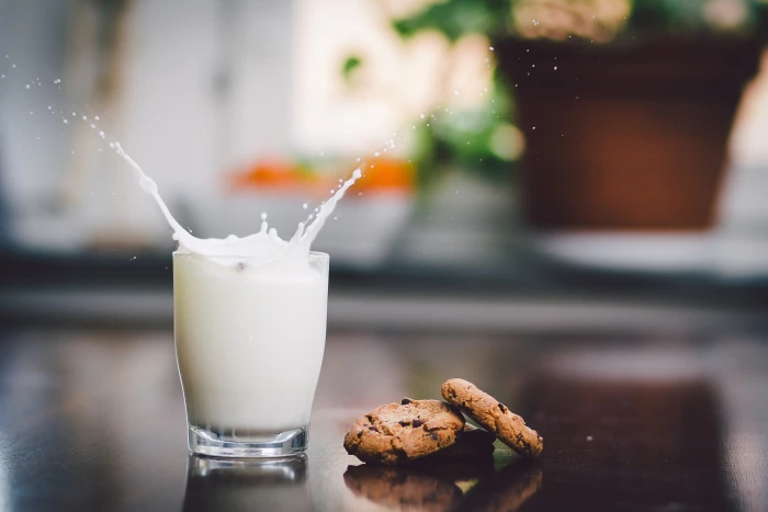 two chocolate dip cookies beside glass of milk splash bokeh 2k 4k 5k