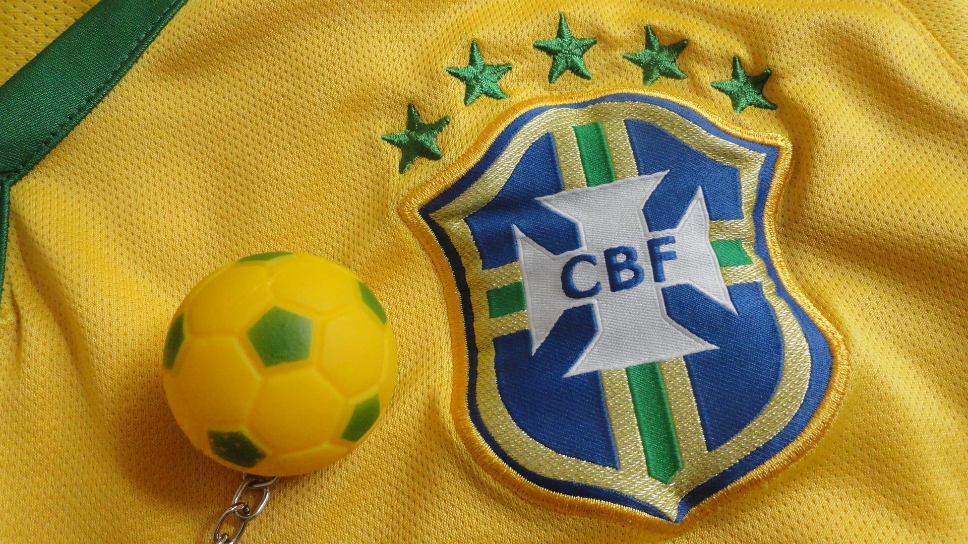 close up photography of soccer ball keychain on yellow CBF jersey shirt