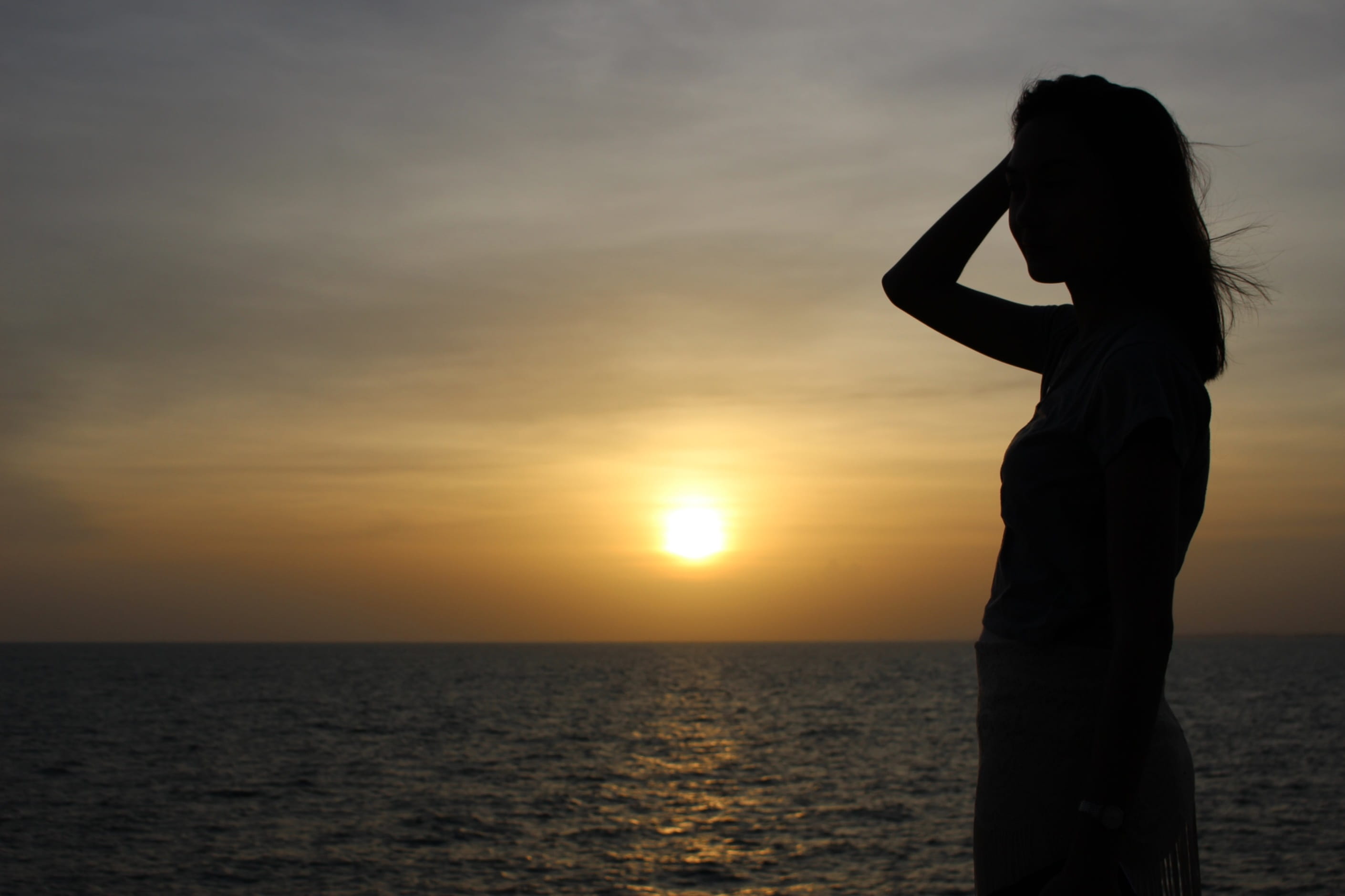 Silhouette of the profile a slim young woman by sea at sunset 2k