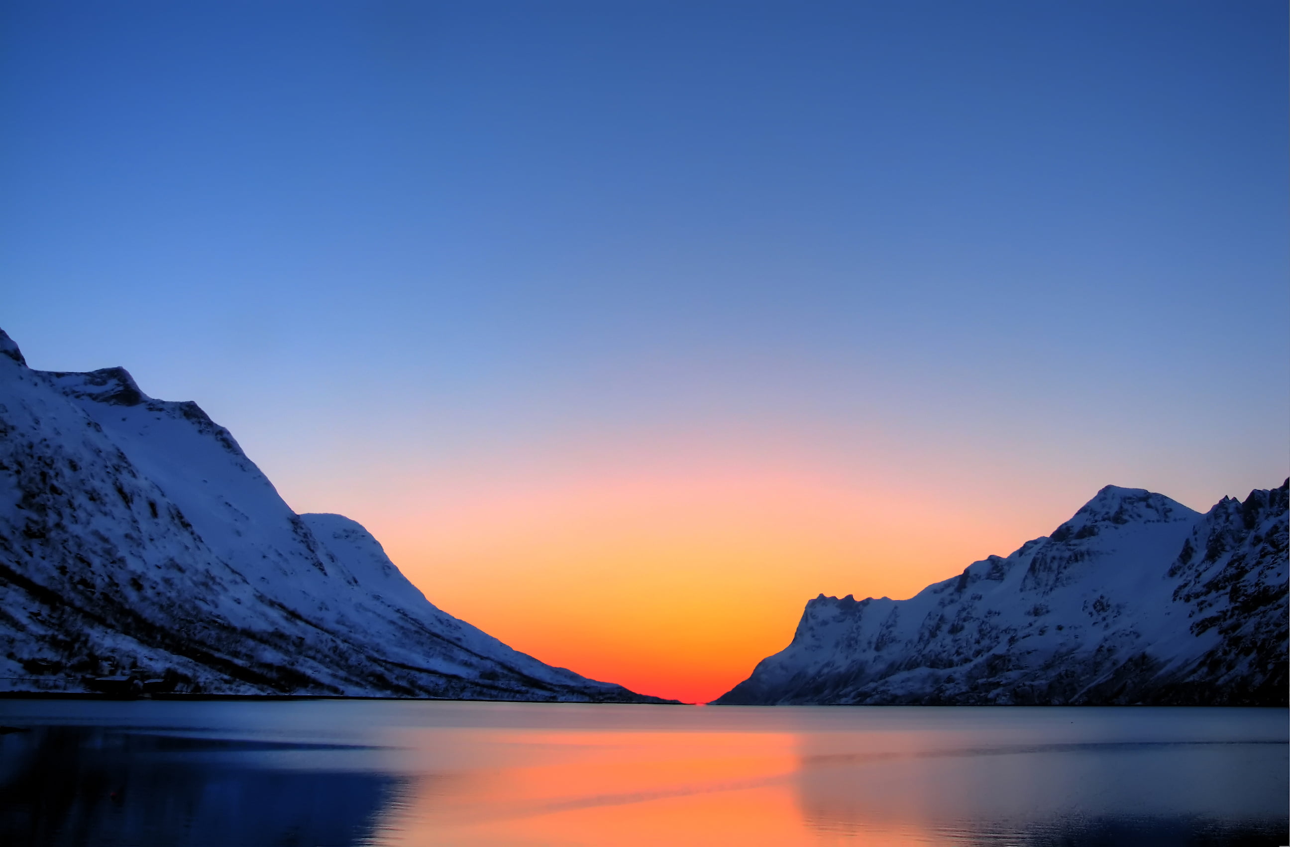 body of water surrounded by snow covered mountains during sunset 2k