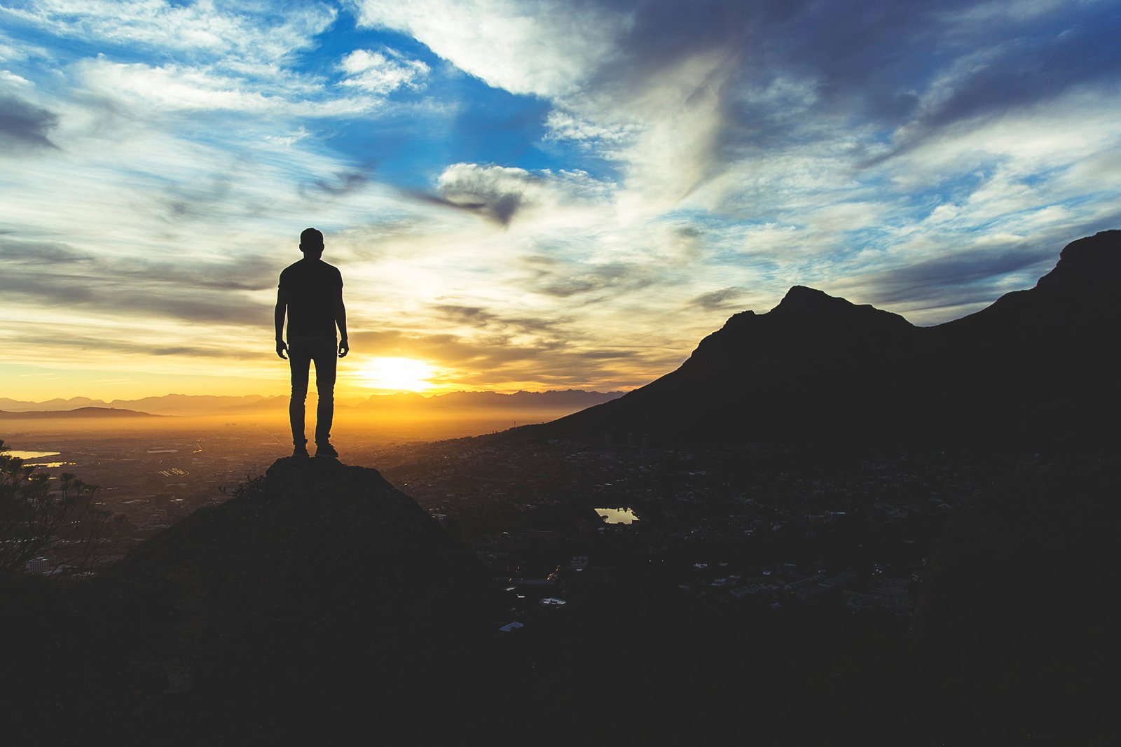 person standing at the top of mountain silhouette photography man on cliff during golden hour 2k