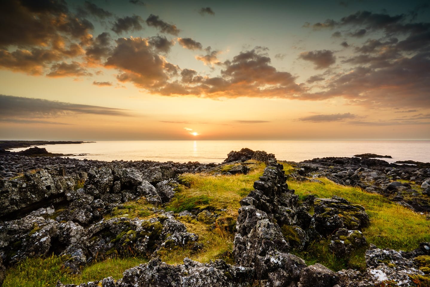 gray rocks and green grass ground near body of water under white cloudy sky during sunset