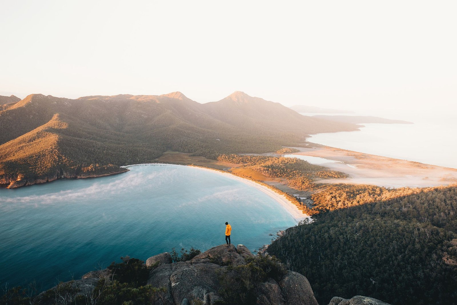 person standing on hill facing body of water and mountain during daytime 2k