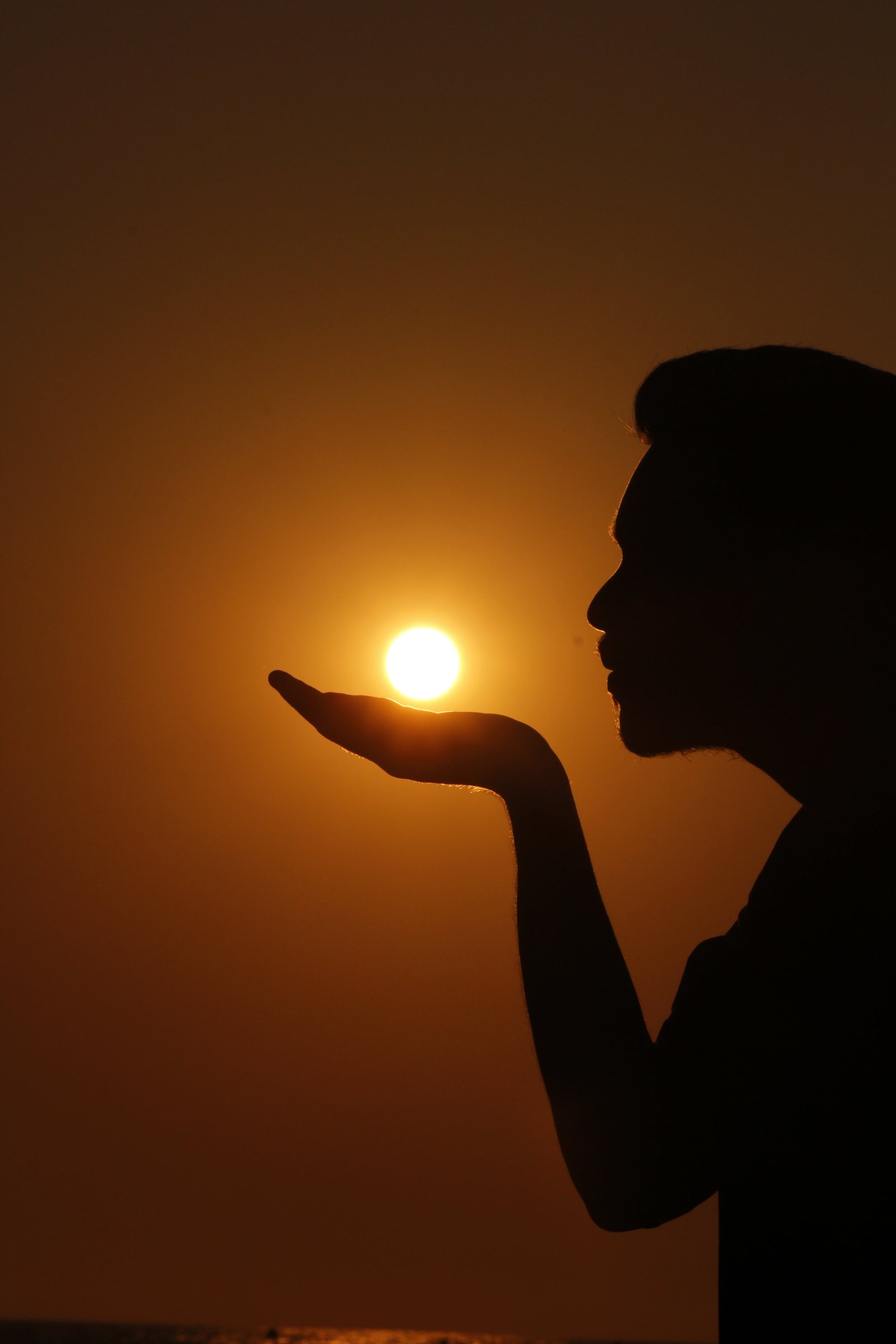 silhouette of a person as if he she is summoning the sun on his her hand 2k