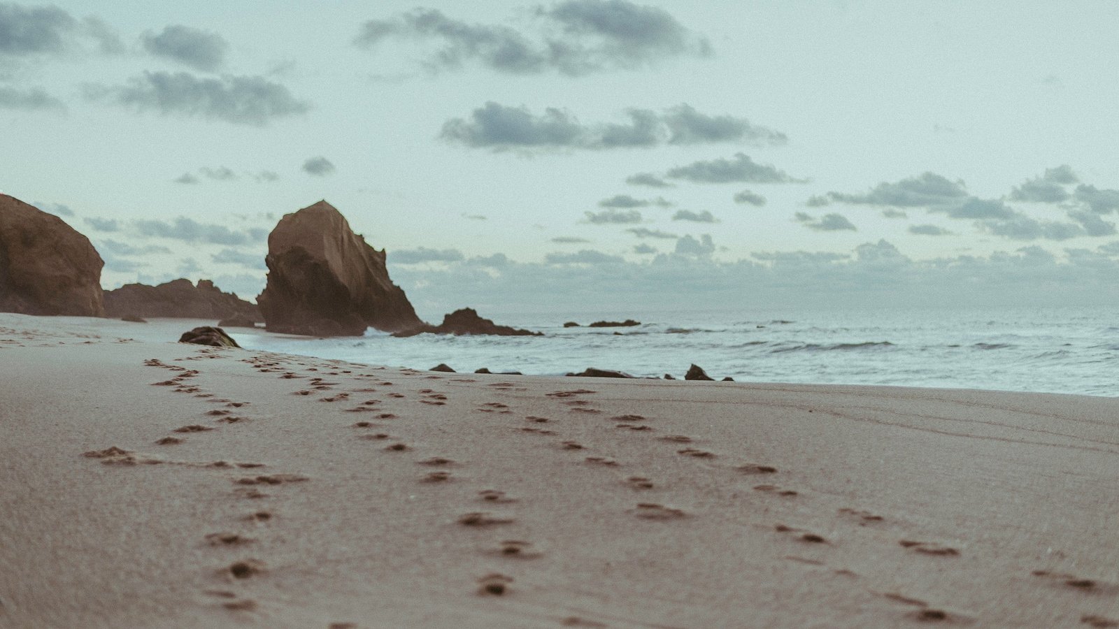 grey sand beach footprints rock sea water land sky object 2k