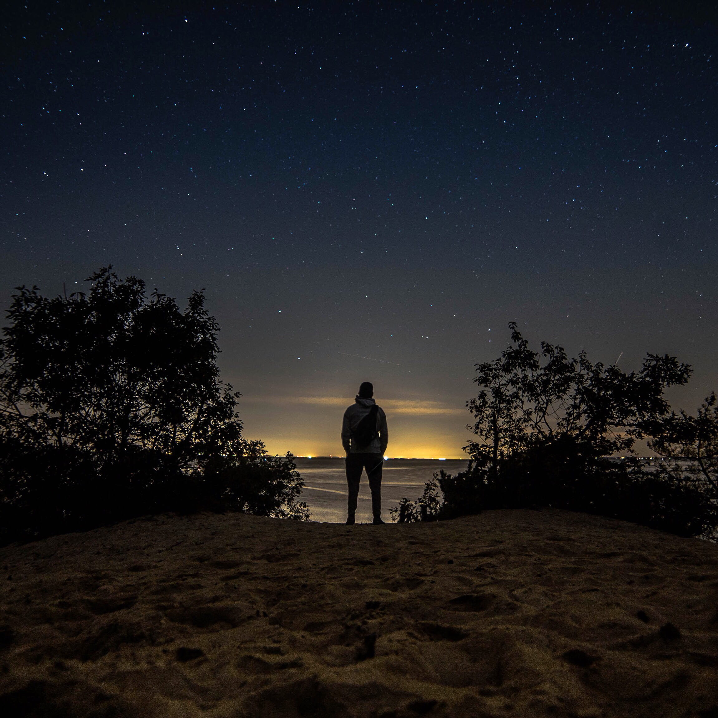 man standing in front of body water staring at the desert under starry night 2k