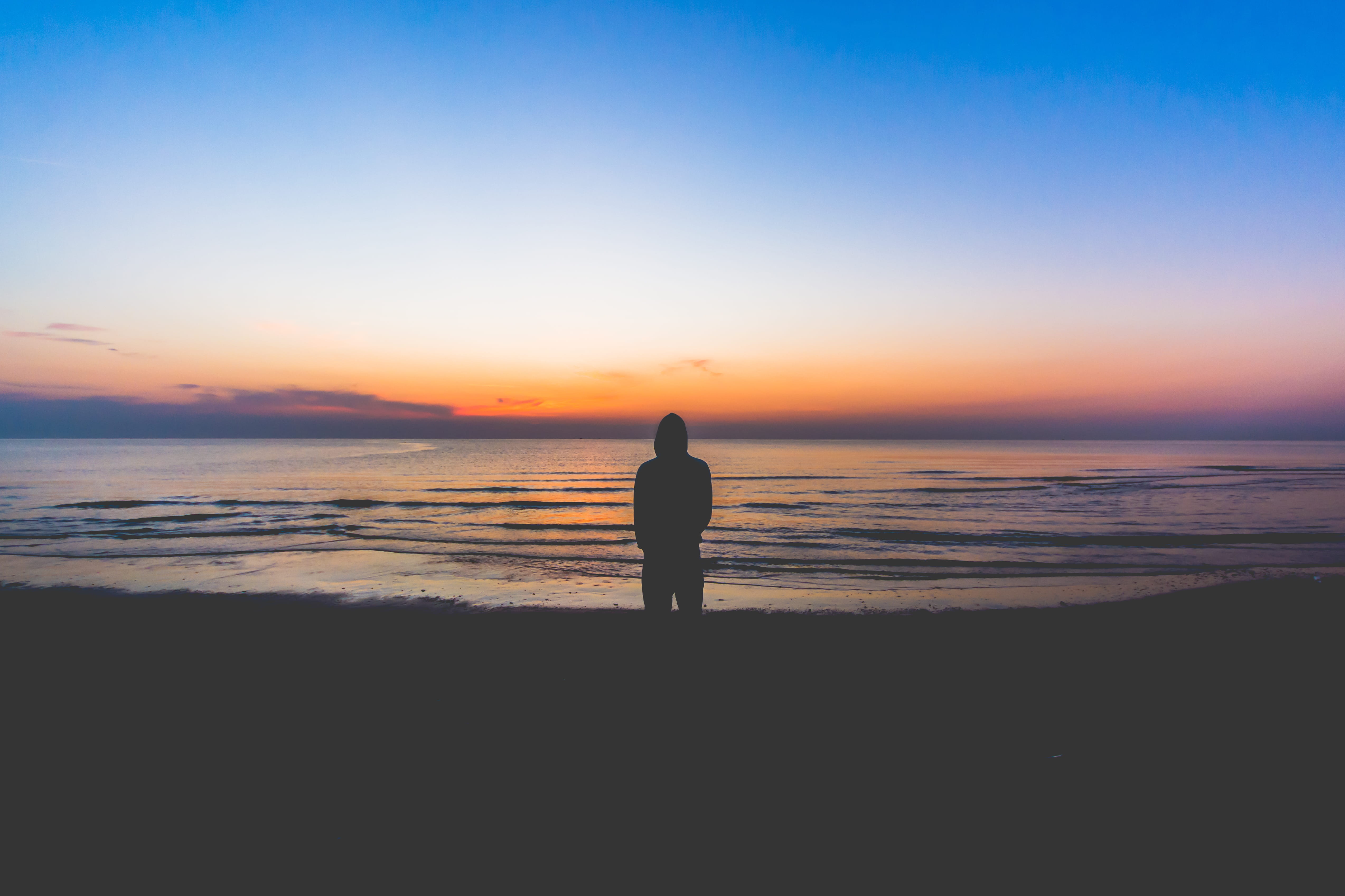 silhouette of person standing near sea during golden hour man wearing hoodie on seashore painting 2k 4k 5k