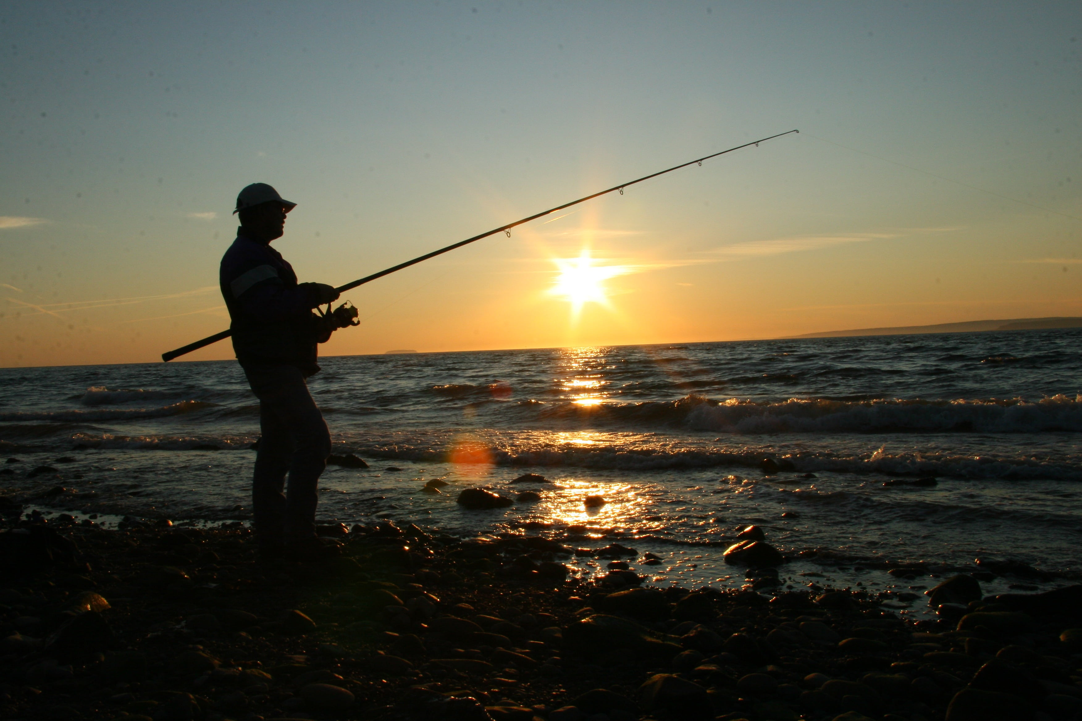 silhouette of person holding fishing rod on beach shore during sunset 2k 4k