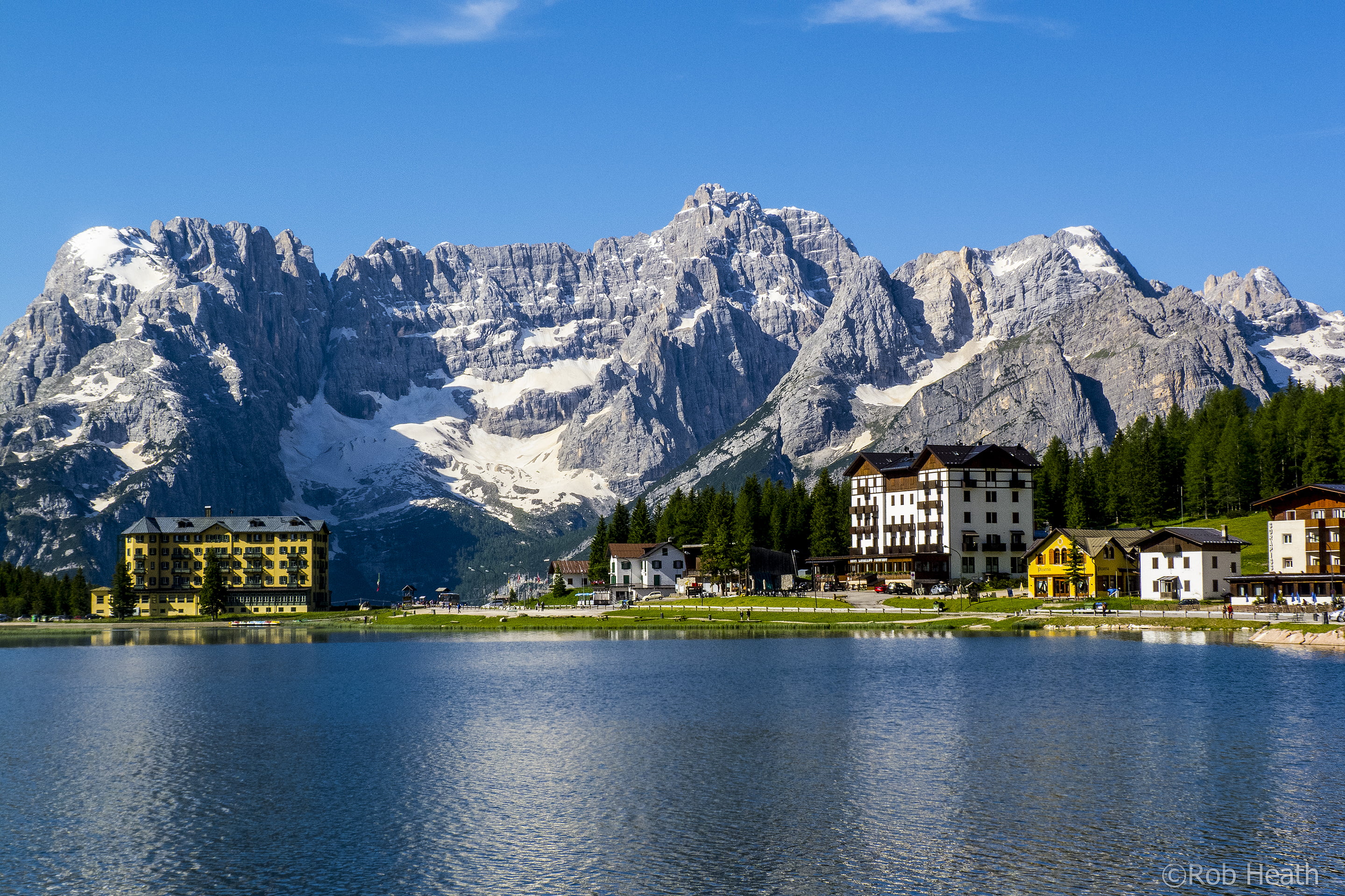 landscape photo of concrete buildings behind the mountains near body water lake misurina 2k