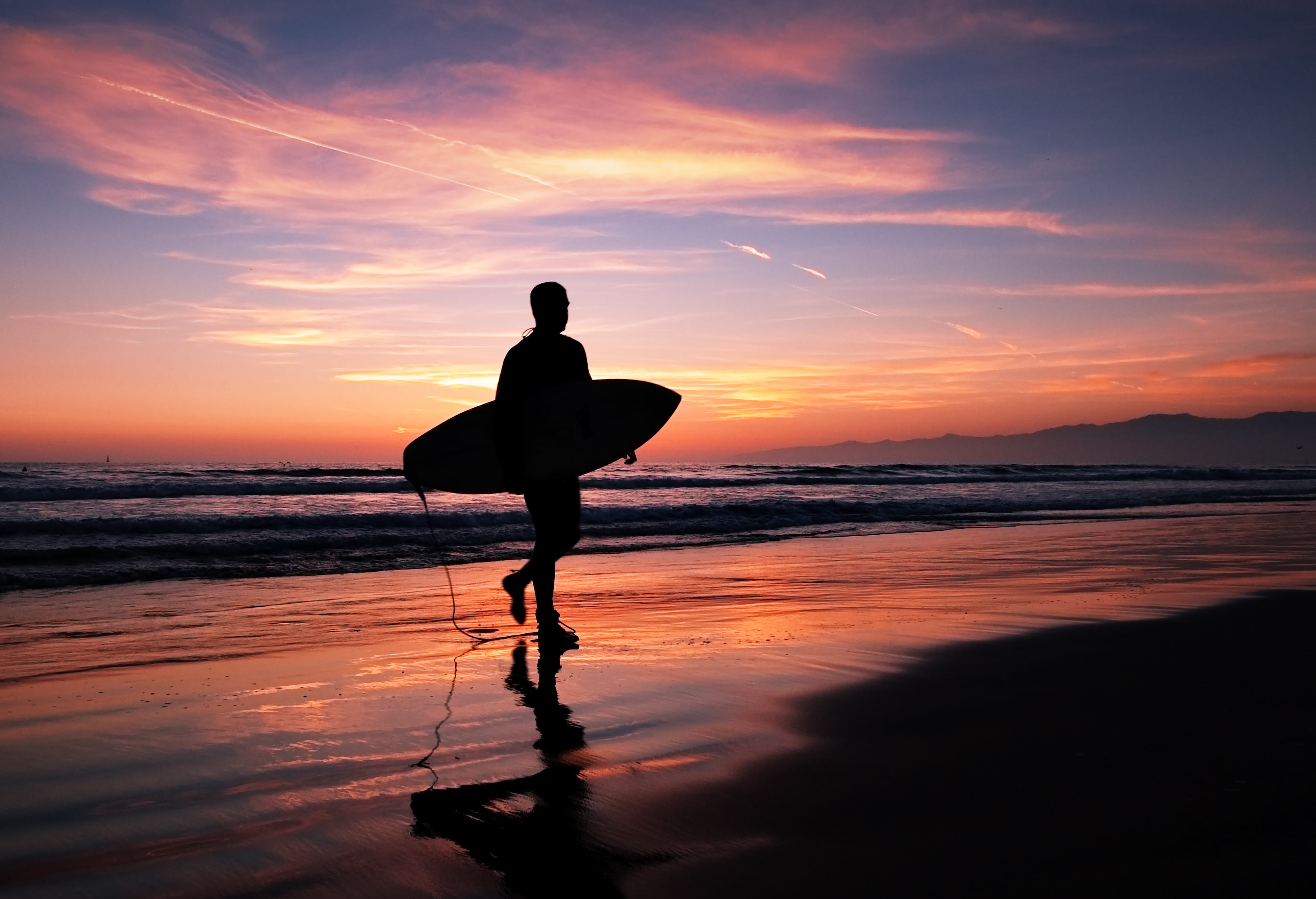 person holding surfboard while walking in the beach at night time los angeles 2k 4k