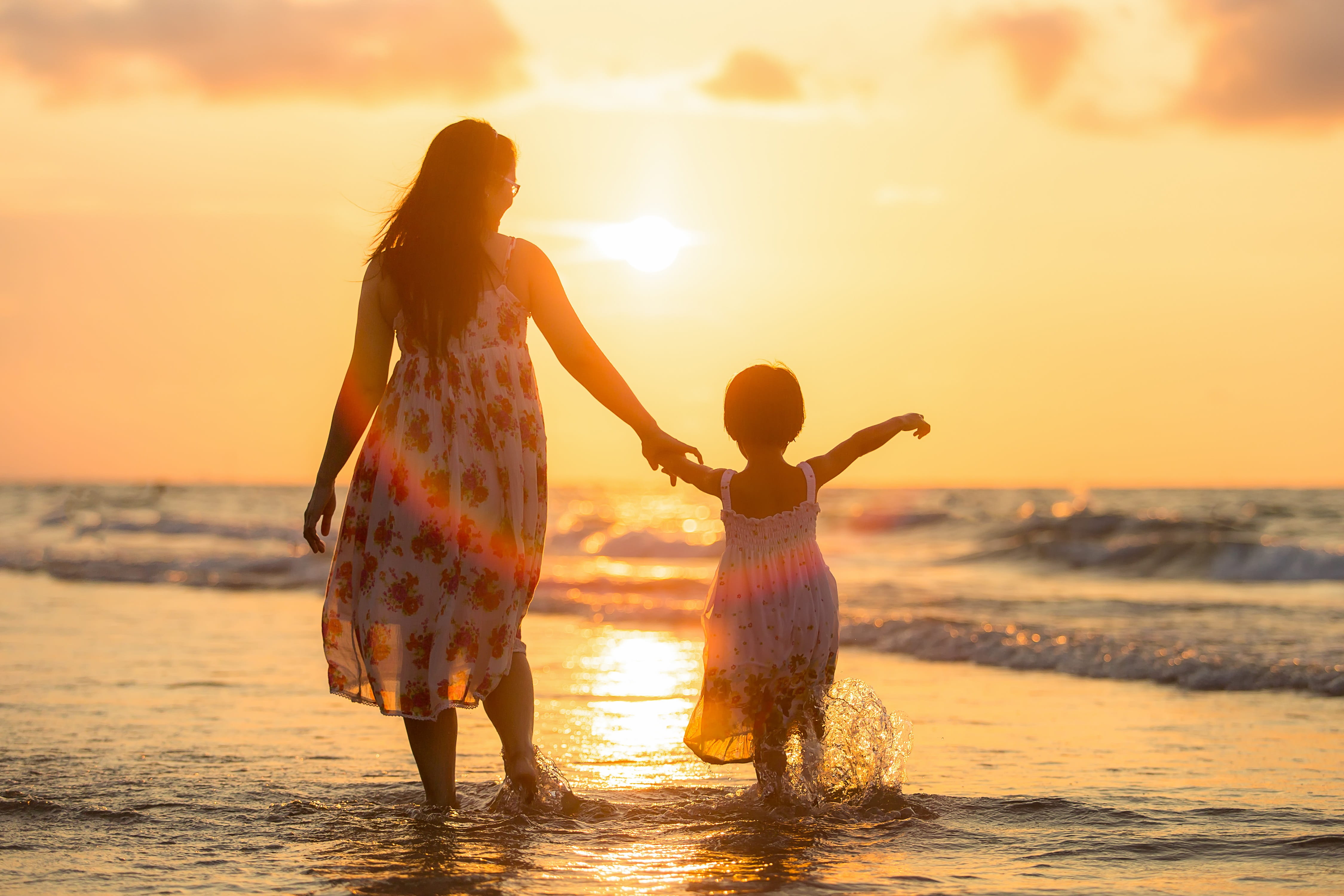 woman wearing white and red sleeveless dress walking with girl on sea shore during sunset 2k 4k 5k