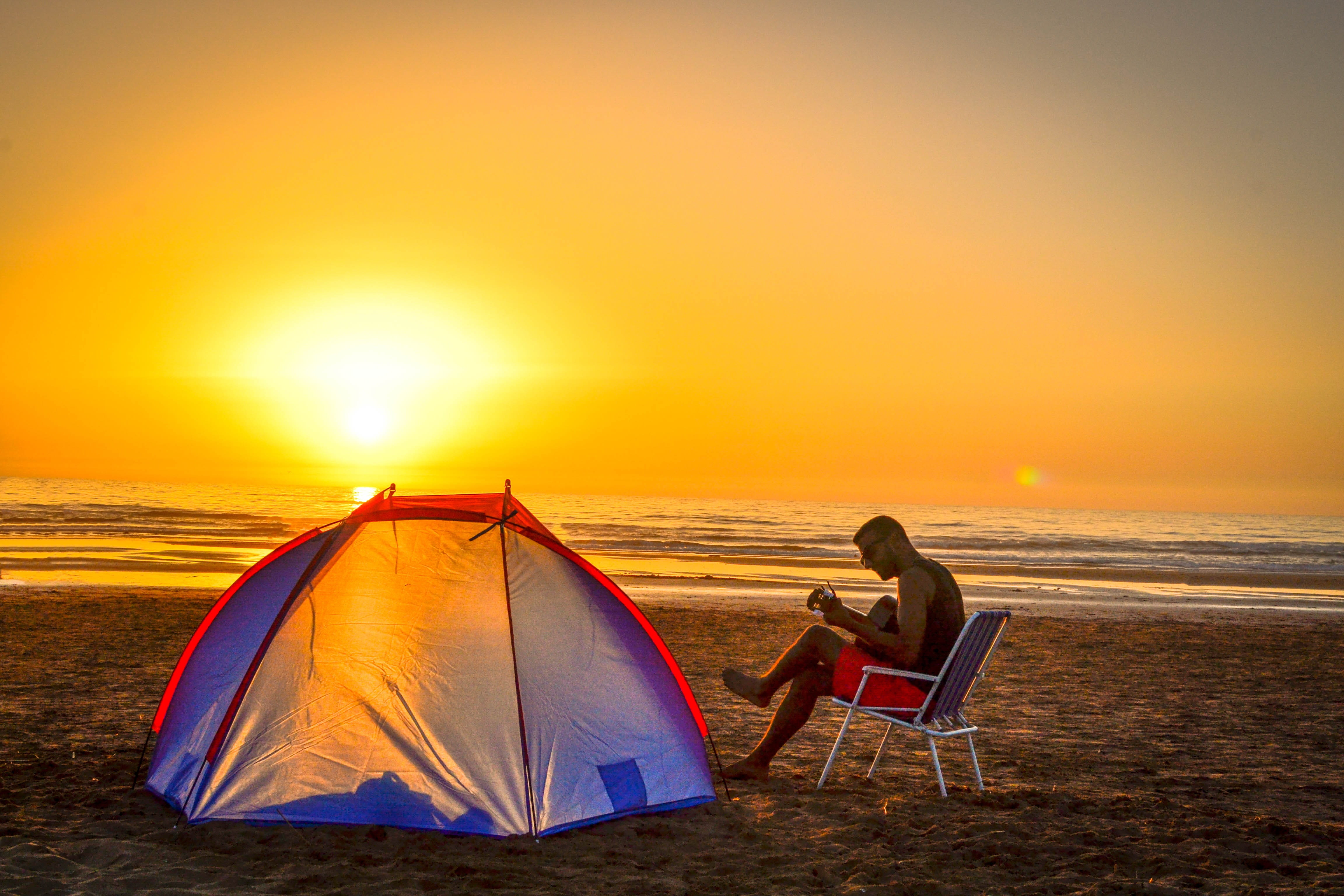 man sitting on chair playing guitar near tent beach shore during sunset 2k 4k 5k