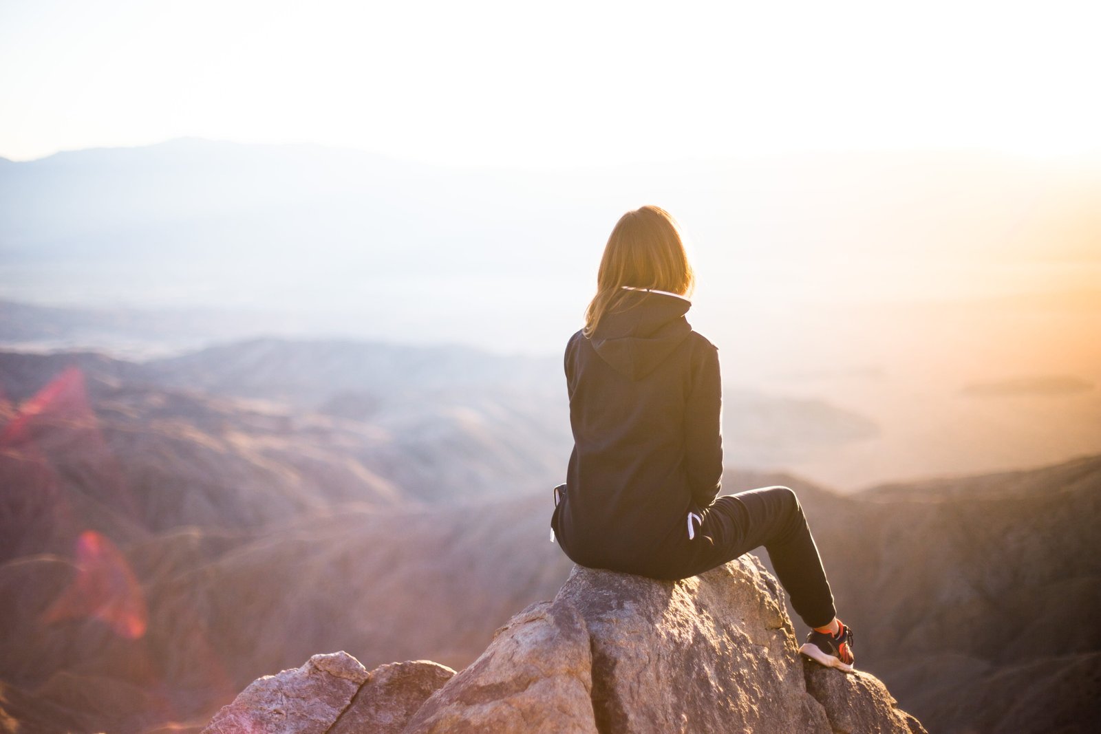 person sitting on top of gray rock overlooking mountain during daytime selective focus photography woman in track suit cliff 2k 4k 5k