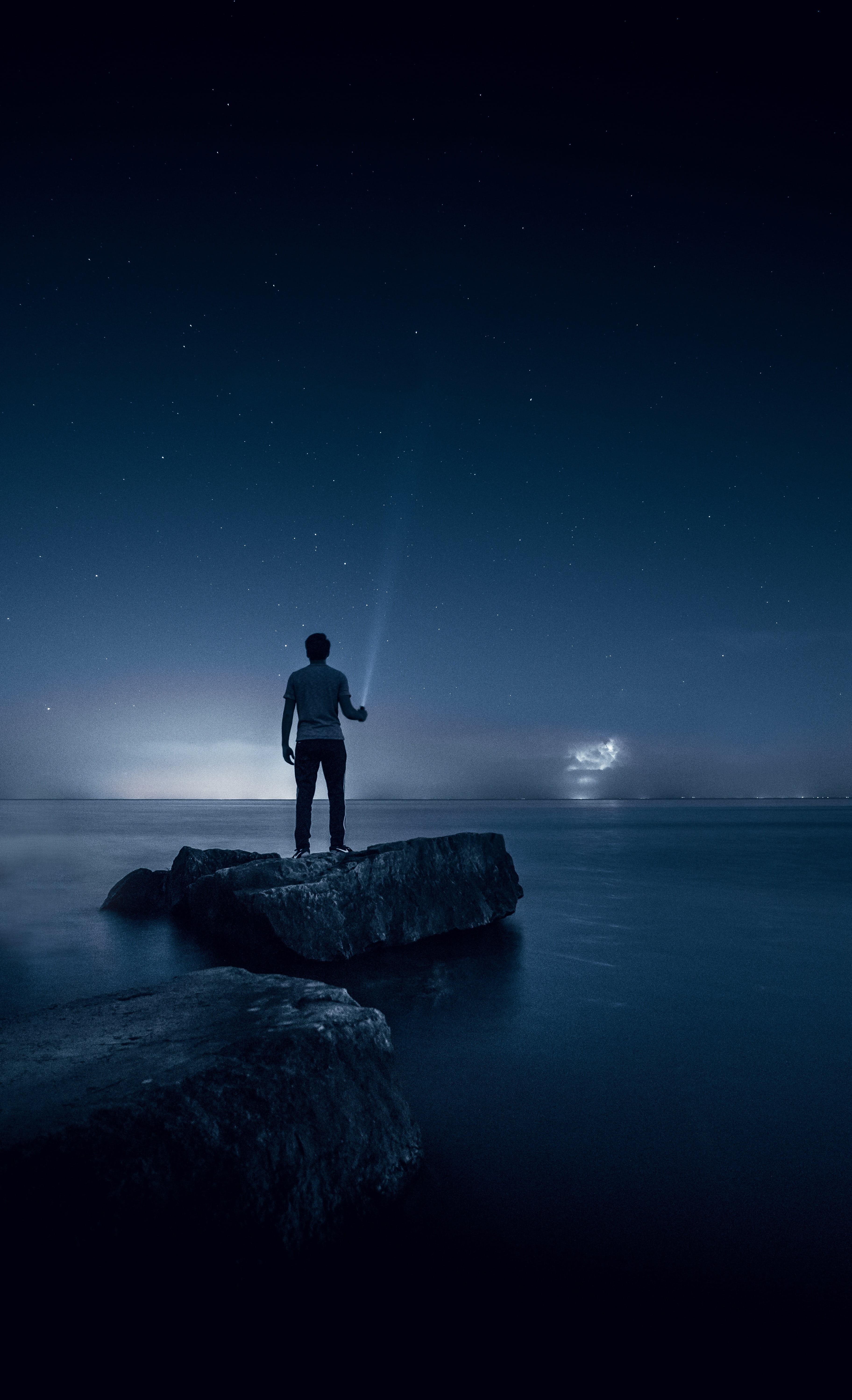 man standing on rock surrounded by water holding a flashlight pointing at the sky 2k 4k
