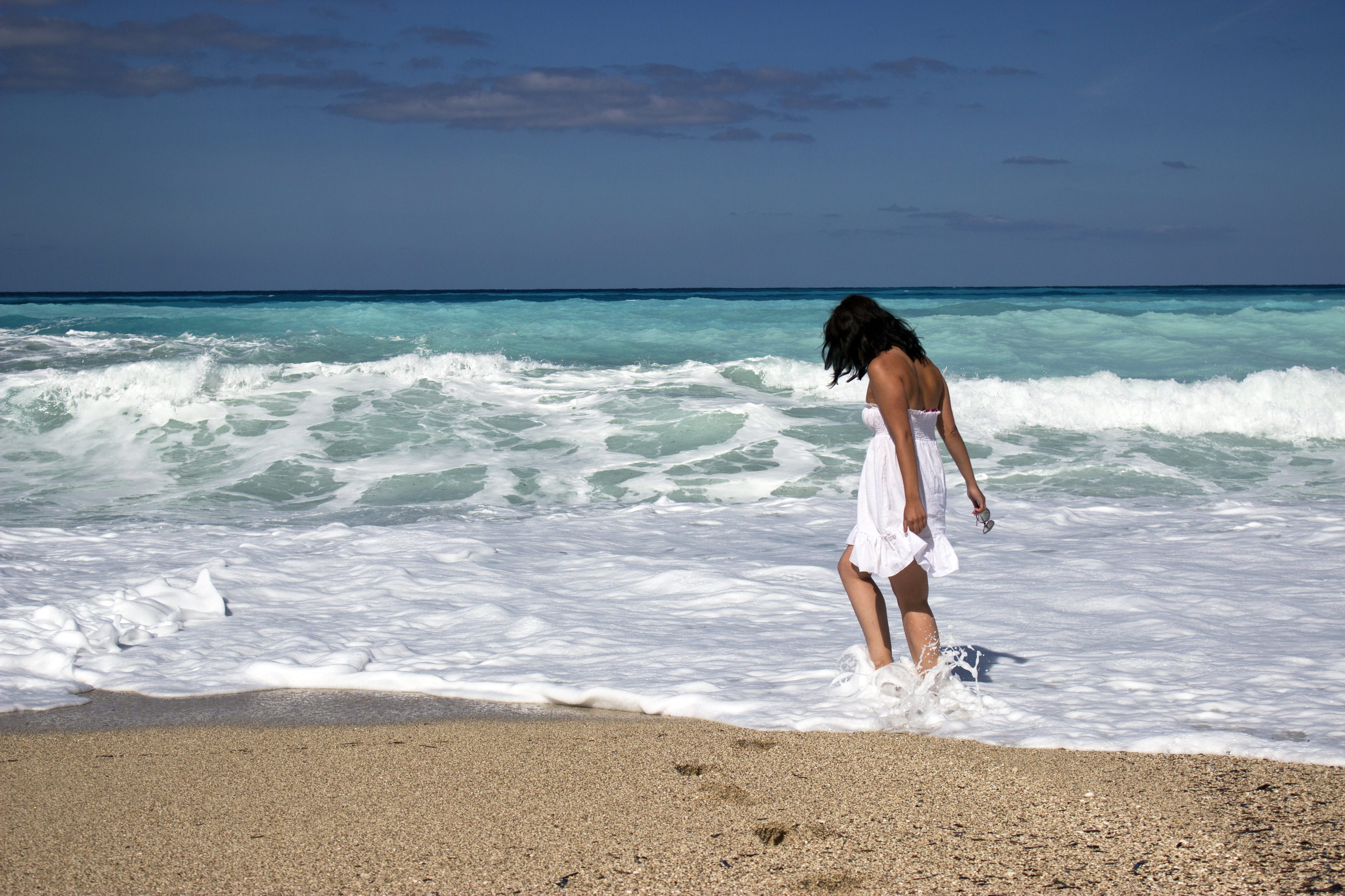 woman in white tube flare mini dress walking on seashore under blue sky during daytime 2k 4k 5k