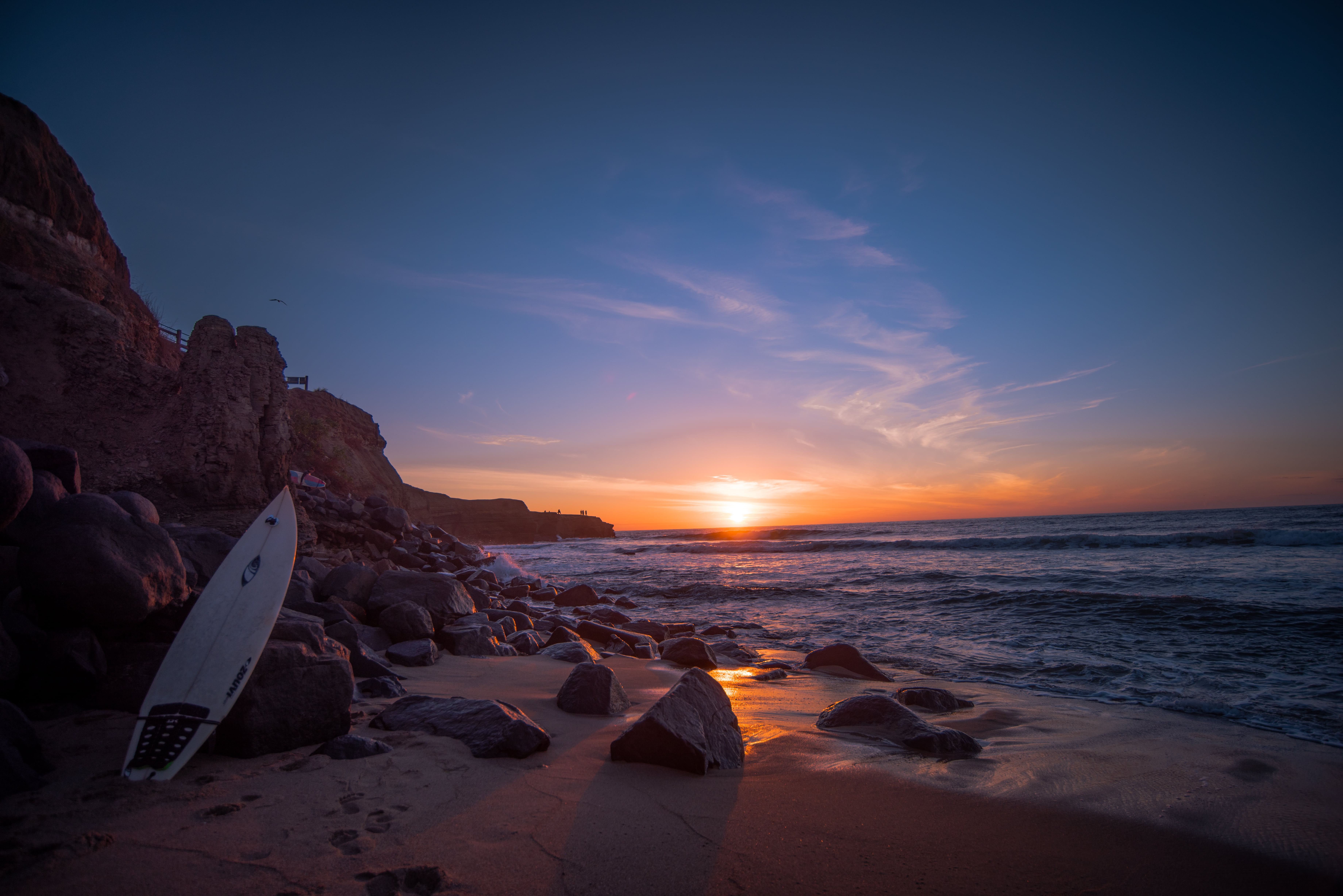 white surfboard leaning on rock near water at sunset Time San 2k 4k 5k
